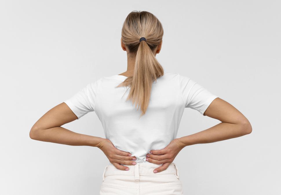 Woman in white shirt holding back because of back pain.