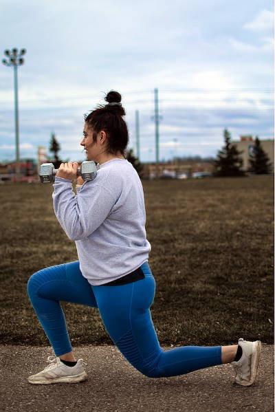 Woman using weights to do lunges outside.